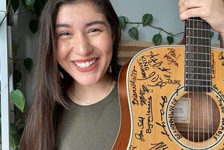 Joelle Montoya holding up a guitar covered with signatures