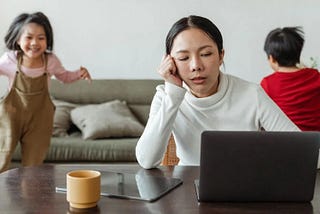 Stressed woman working on computer with kids running around in background