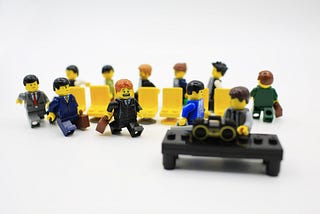 IMAGE: Mini-Lego figures dressed as executives and playing a game of musical chairs