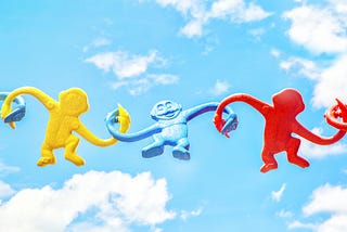 A photo of three colourful plastic toy monkeys holding hands on a bright day