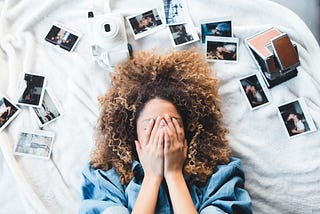 A girl lying on the floor with hands over her face and printed photos surrounding her.