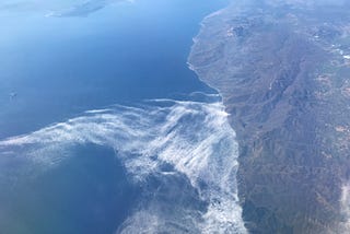 A view of land, sea and clouds from airplane window while traveling.