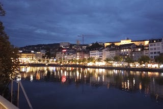 Early evening on the riverfront in Zurich, Switzerland with the lights from the town reflecting in the water.