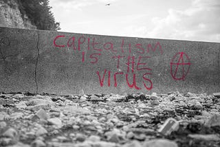 A grayscale image that shows a wall with red text graffitti. It says: Capitalism is the virus.