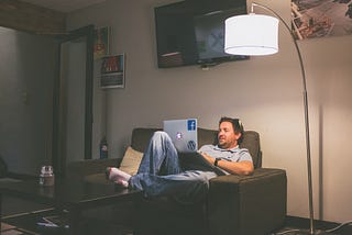Man sitting on his sofa in a low-lit room with his laptop on.