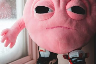 A pink brain with sad eyes and a frown, wearing sneakers and standing on a windowsill.