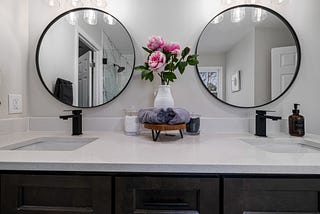 White bathroom sink with double black taps and mirrors