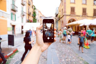 man holding a phone with the camera facing a busy old street