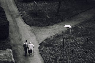 A man walking beside an old woman on a road.