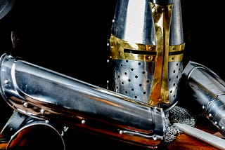 Pic of a silver medieval knight’s armor with gold-shaped cross on the helmet.