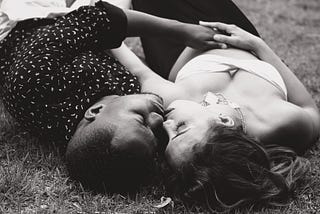 A mixed race couple, pictured from above, lying on the grass embracing