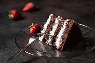 Slice of chocolate layer cake with cream frosting between layers, a few strawberries and a fork ready to dif in.