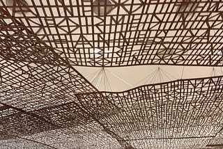 wood latices hanging from the ceiling of a beige foyer.