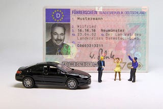 A picture of a drivers license ID card behind a toy car and three toy people