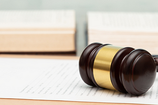 Close up of a wooden gavel on a desk lying in front of an open book.