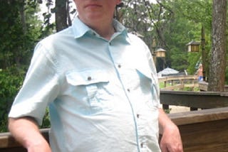 The author standing outside on a wooden walkway wearing a white hat