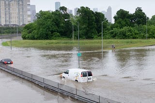 A van driving along a road in Houston, Texas is submerged in water during a flood event.