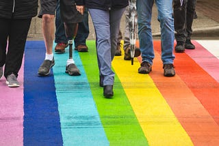 A group of people walking on a road that is painted rainbow colors