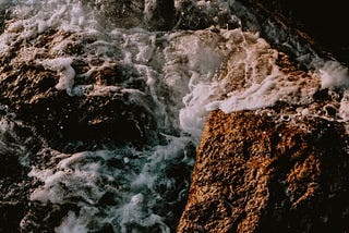 A warm close-up photo of rocks bathed in frothy seawater.