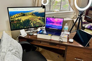 Multi-monitor setup with Macbook Air and iPad Pro with two ring lights, mouse, water bottle, headsets, and iPhone cradle