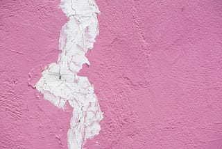 An close up of a wall panted pink with spackle filling in a large crack