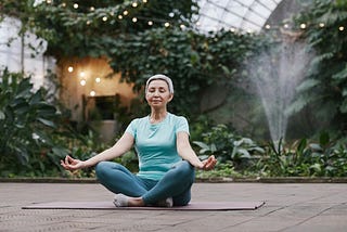 Middle-aged woman with short hair meditating on a yoga mat in a relaxing garden.