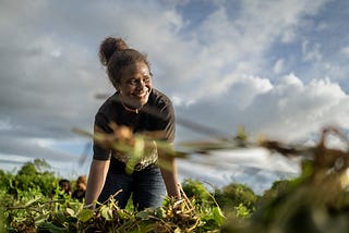 Woman standing in a field smiling up with the sky behind her