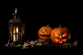 a lantern with a burning candle and two Halloween carved pumpkins with scary faces