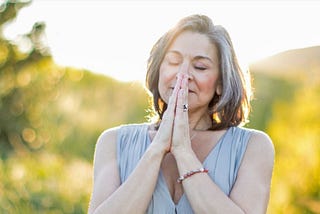 Donna Bond eyes closed with hands in prayer position in sun