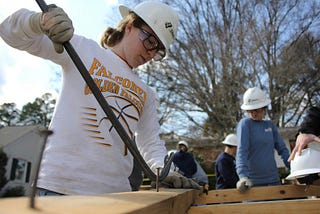 Woman in hard hat and gloves uses crow bar on a nail in lumber