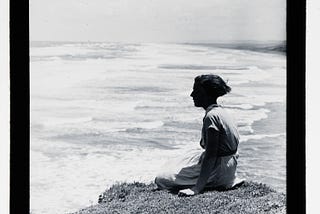 A woman sites on a cliff overlooking Muriwai beach