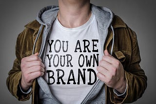 Man holding jacket open to show a t-shirt that says “You are your own brand”