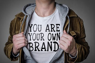 Man holding jacket open to show a t-shirt that says “You are your own brand”