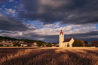 A village with a church and a field in the foreground.