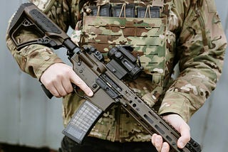 Torso of a paramilitary in standard army attire, holding a semi-automatic rifle across his body.