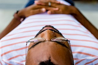 A man in a striped shirt lies on the ground while meditating.