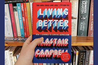 The author holding Living Better by Alastair Campbell, with a book shelf in the background