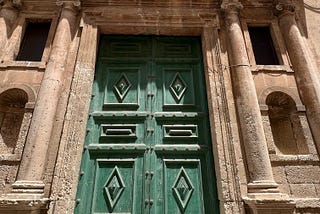 A large, green, ornate door to a baroque Sicilian building