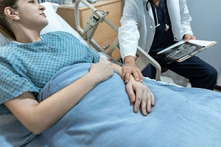 A doctor touches his bedridden patient’s arm.