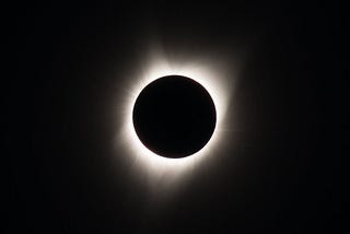 An eclipse where the sun is shining its light around the moon blocking it.