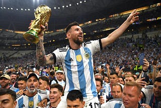 Messi segura o trófeu Copa do Mundo FIFA enquanto é carregado nos ombros em meio a multidão