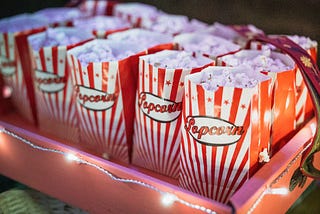 A large red tray outlined with lights holding three rows of movie popcorn in red and white paper bags.
