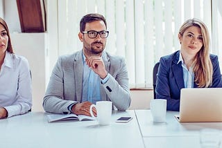 Trzy osoby prowadzące rozmowę siedzą przy stole naprzeciw kandydata, ilustracja do tematu co zabrać na rozmowę kwalifikacyjną.