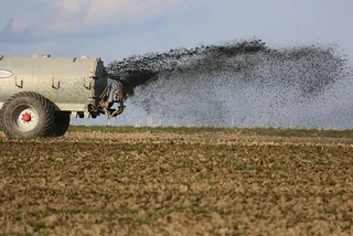 Sludge spreader applying sewage sludge on a farm.