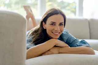 A smiling woman lying on a couch at home.