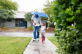 A man and young girl walk with an umbrella.