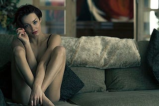 A beautful undressed woman with short brunette hair seated on a gray sofa