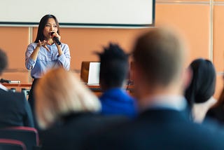 An Asian woman presenter interacting with the audience at a business presentation in the board room.