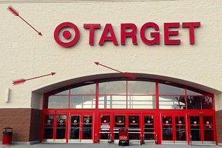 A Target store entrance is shown with the brand name prominently displayed above red double doors. Several red arrows have been added to the image, pointing at the bullseye logo. The arrows emphasize the play on the word “Target.”