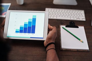 picture of desk and on it is tablet with bar graph on it, pencil and paper, and keyboard